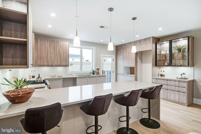 kitchen with pendant lighting, a kitchen breakfast bar, light hardwood / wood-style floors, backsplash, and light stone counters