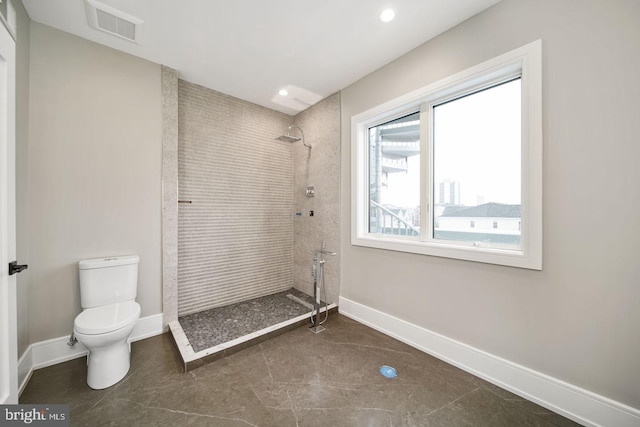 bathroom with toilet, tiled shower, and tile floors