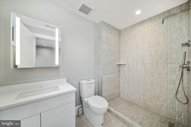 bathroom with toilet, a tile shower, and vanity