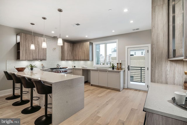 kitchen with light stone countertops, tasteful backsplash, decorative light fixtures, and light wood-type flooring