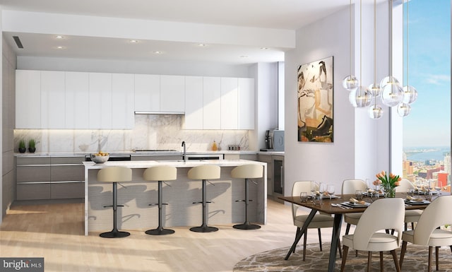 kitchen featuring white cabinets, a breakfast bar, light hardwood / wood-style floors, a center island with sink, and tasteful backsplash