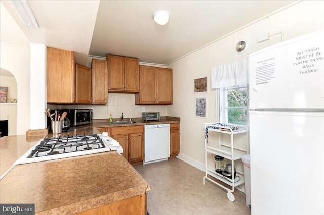 kitchen with white appliances, tasteful backsplash, sink, and a brick fireplace