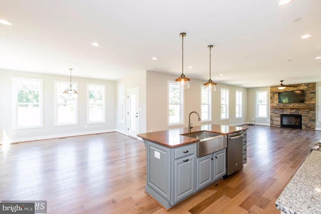 kitchen featuring a center island with sink, stainless steel dishwasher, light wood-type flooring, a fireplace, and sink