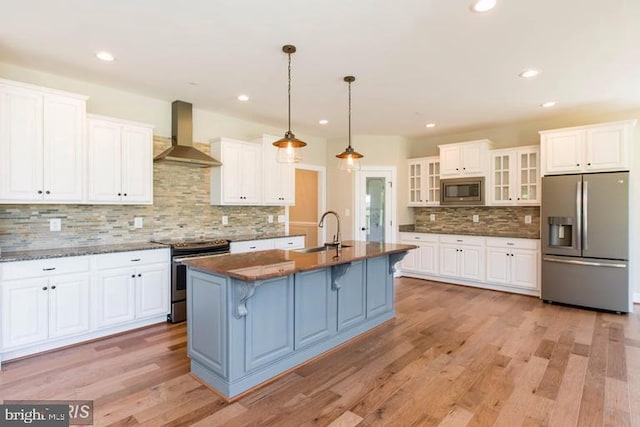 kitchen with sink, light hardwood / wood-style floors, stainless steel appliances, wall chimney exhaust hood, and white cabinetry