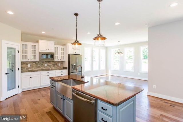 kitchen featuring appliances with stainless steel finishes, pendant lighting, white cabinetry, and a kitchen island with sink