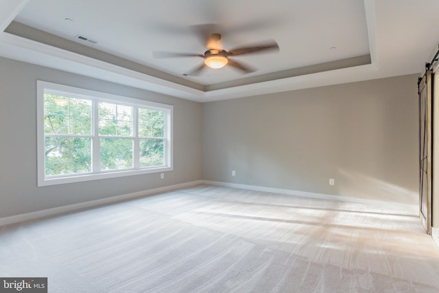 carpeted empty room featuring a barn door, ceiling fan, and a tray ceiling