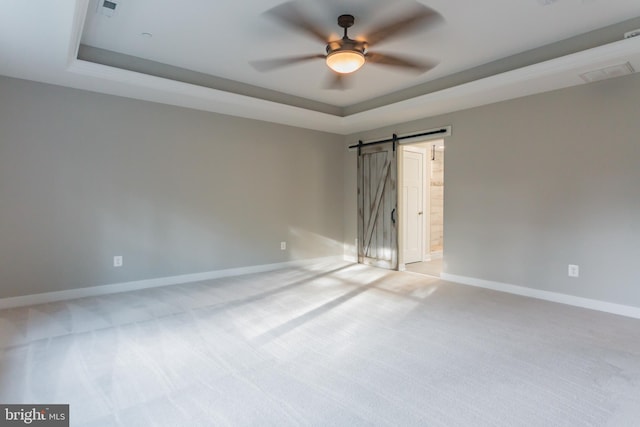 empty room with a barn door, a raised ceiling, light carpet, and ceiling fan