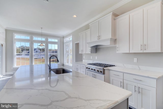 kitchen with light stone counters, white cabinetry, crown molding, stainless steel gas stovetop, and hanging light fixtures