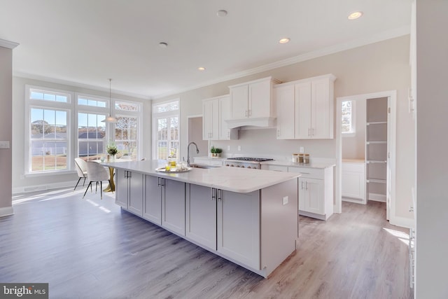 kitchen featuring a kitchen island with sink, white cabinets, pendant lighting, and light wood-type flooring