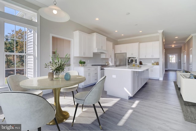 kitchen with stainless steel fridge, light hardwood / wood-style floors, an island with sink, white cabinets, and pendant lighting