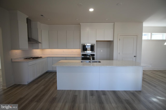 kitchen with dark wood-type flooring, a center island with sink, wall chimney range hood, white cabinetry, and stainless steel appliances