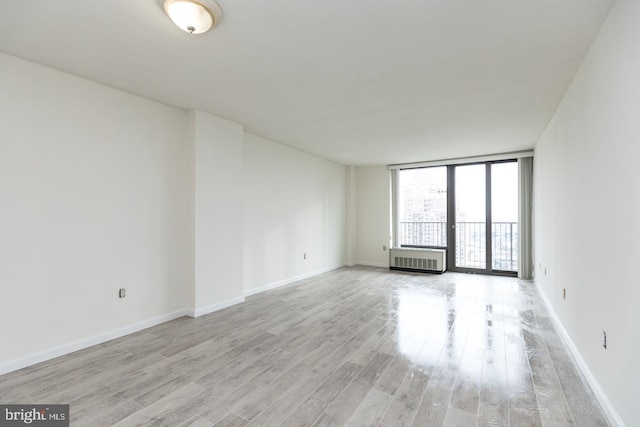 spare room with floor to ceiling windows, radiator heating unit, and light wood-type flooring