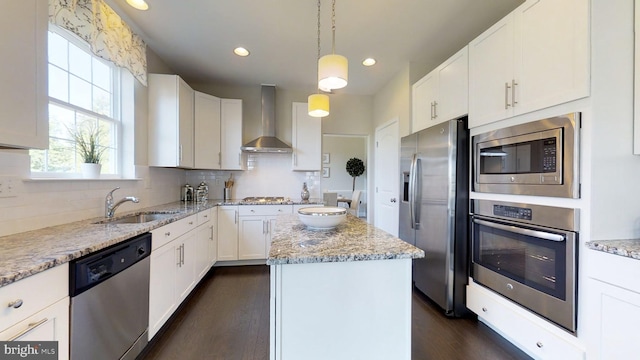 kitchen with stainless steel appliances, decorative light fixtures, a kitchen island, wall chimney range hood, and white cabinets