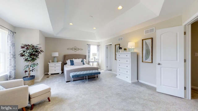 bedroom with light colored carpet and a tray ceiling