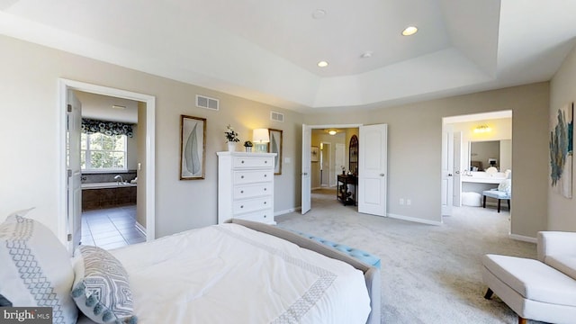 bedroom with a raised ceiling, light colored carpet, and ensuite bath