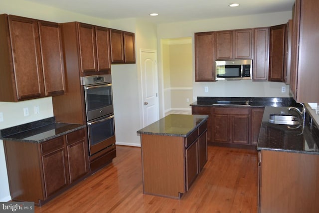 kitchen featuring sink, dark stone counters, a kitchen island, hardwood / wood-style floors, and appliances with stainless steel finishes