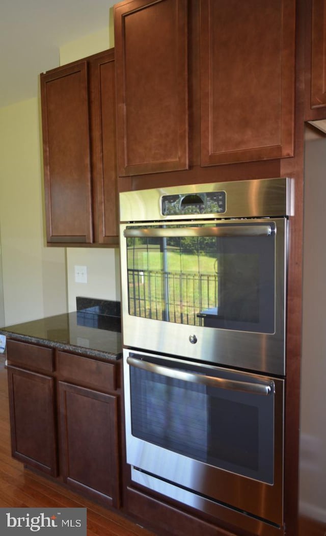 kitchen with dark stone counters, double oven, and dark hardwood / wood-style floors