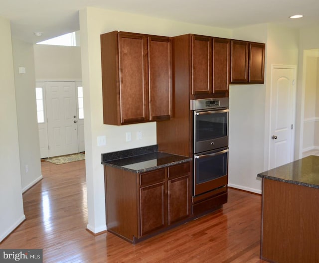 kitchen with hardwood / wood-style floors, stainless steel double oven, dark stone countertops, and a healthy amount of sunlight