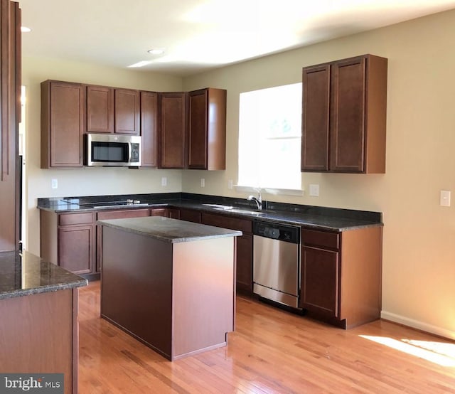 kitchen featuring appliances with stainless steel finishes, light hardwood / wood-style flooring, dark stone countertops, a center island, and dark brown cabinetry