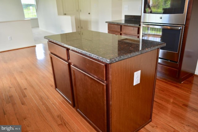 kitchen featuring double oven, a kitchen island, light hardwood / wood-style flooring, and dark stone countertops