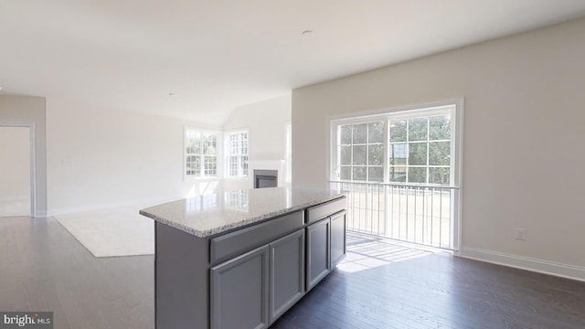 kitchen featuring light stone countertops, a center island, dark wood-type flooring, and a wealth of natural light