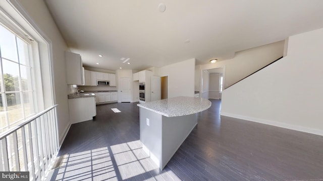 kitchen featuring dark wood-type flooring, appliances with stainless steel finishes, white cabinets, a center island, and sink