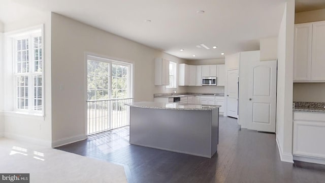 kitchen featuring a kitchen island, light stone countertops, dark hardwood / wood-style flooring, white cabinets, and sink