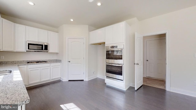 kitchen with dark hardwood / wood-style flooring, white cabinetry, stainless steel appliances, and light stone countertops