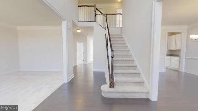 stairway with dark wood-type flooring, ornamental molding, and a towering ceiling