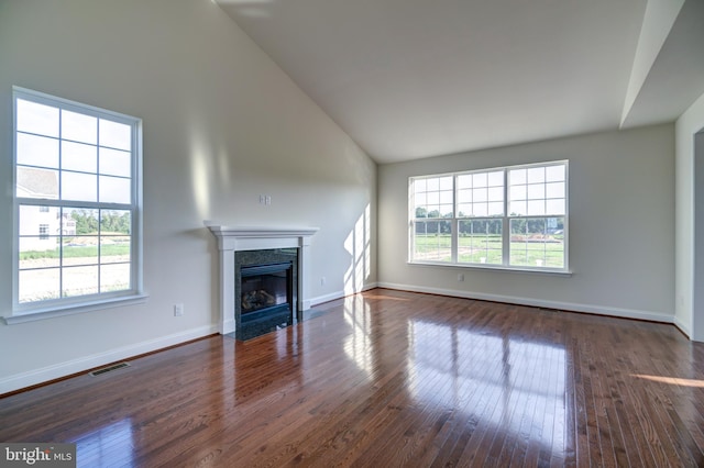 unfurnished living room with high vaulted ceiling, dark hardwood / wood-style floors, a premium fireplace, and a healthy amount of sunlight