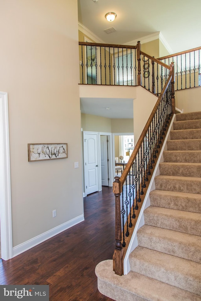 staircase with dark hardwood / wood-style floors, a towering ceiling, and ornamental molding