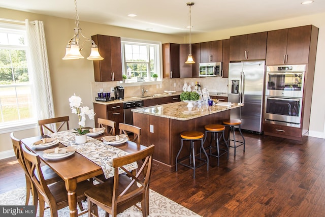 kitchen featuring hanging light fixtures, dark wood-type flooring, appliances with stainless steel finishes, a center island, and light stone counters