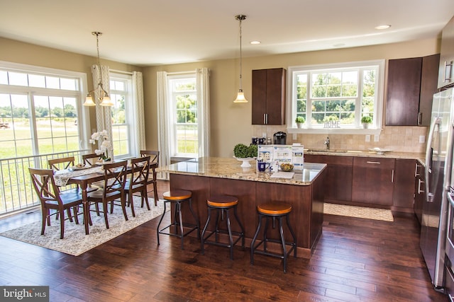 kitchen featuring a wealth of natural light, dark hardwood / wood-style floors, a center island, light stone countertops, and hanging light fixtures