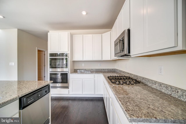 kitchen with white cabinets, appliances with stainless steel finishes, light stone countertops, and dark hardwood / wood-style flooring