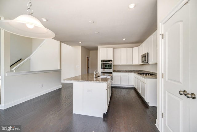 kitchen with light stone countertops, stainless steel appliances, dark hardwood / wood-style flooring, and a kitchen island with sink