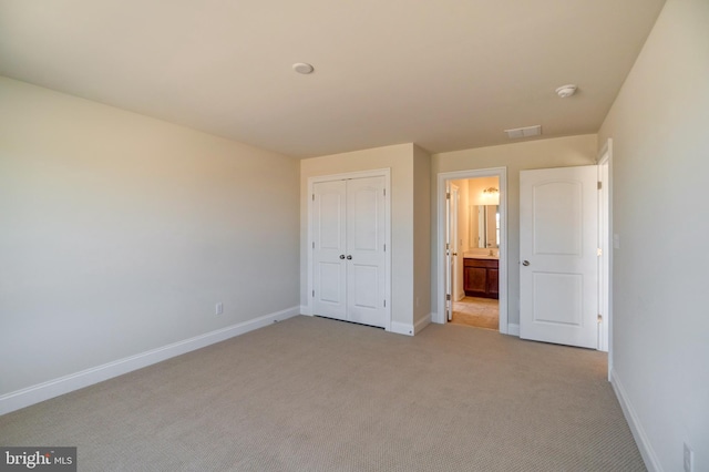 unfurnished bedroom featuring connected bathroom, light colored carpet, and a closet