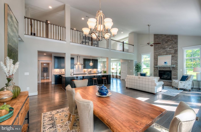 dining space featuring a fireplace, high vaulted ceiling, dark wood-type flooring, and ceiling fan with notable chandelier