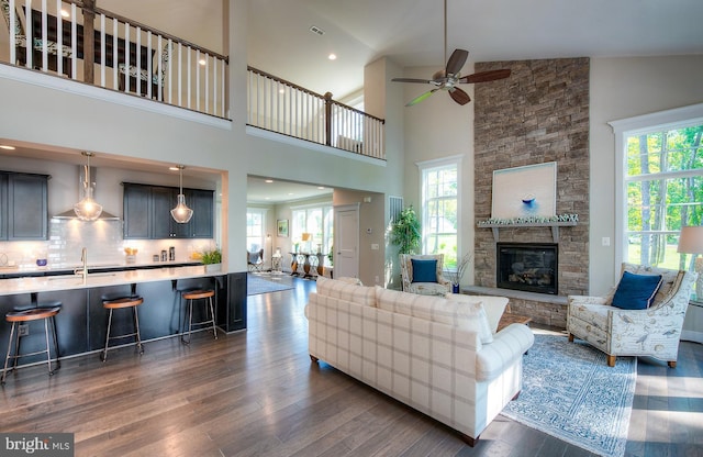 living room with dark hardwood / wood-style flooring, high vaulted ceiling, ceiling fan, and a stone fireplace