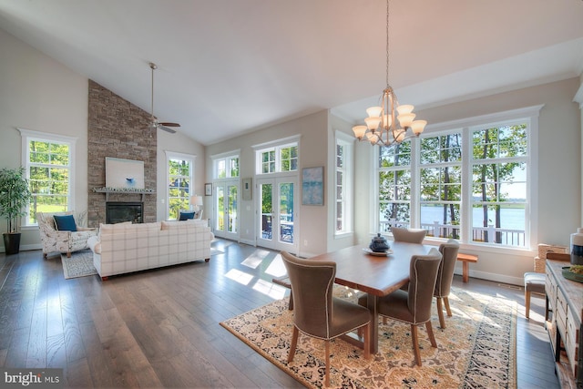 dining room with dark hardwood / wood-style flooring, a stone fireplace, high vaulted ceiling, and a healthy amount of sunlight