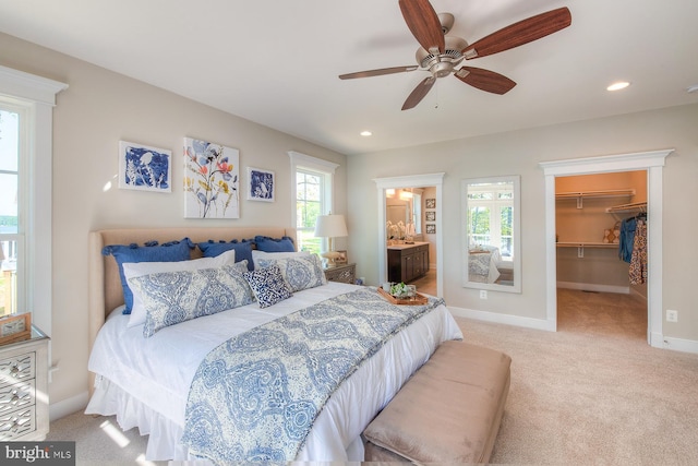 bedroom featuring a walk in closet, multiple windows, ceiling fan, and light colored carpet