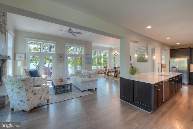 living room with dark hardwood / wood-style flooring, ceiling fan with notable chandelier, a healthy amount of sunlight, and a stone fireplace