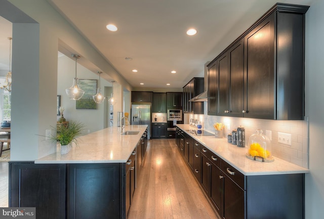 kitchen with hanging light fixtures, light stone counters, backsplash, black electric cooktop, and light hardwood / wood-style flooring