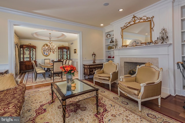 living room with a notable chandelier, ornamental molding, built in shelves, and wood-type flooring