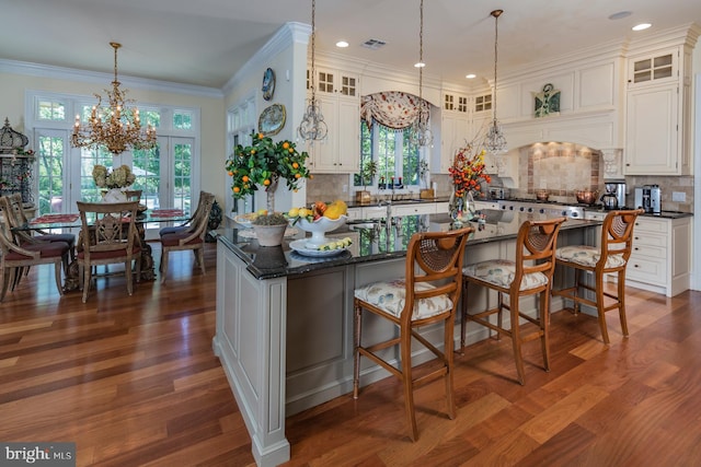 kitchen with backsplash, a kitchen island with sink, dark hardwood / wood-style floors, and an inviting chandelier