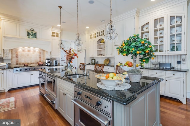 kitchen with an island with sink, appliances with stainless steel finishes, white cabinets, decorative light fixtures, and hardwood / wood-style flooring