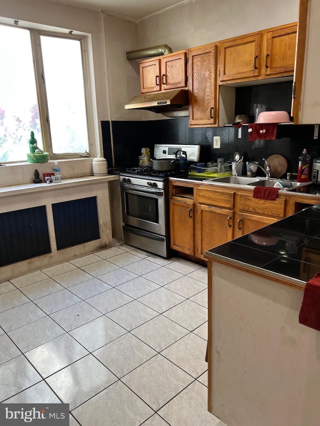 kitchen with gas stove, tasteful backsplash, light tile floors, tile countertops, and sink