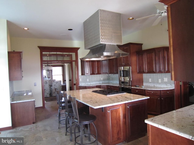 kitchen with ceiling fan, ventilation hood, a kitchen island, a kitchen breakfast bar, and light stone countertops