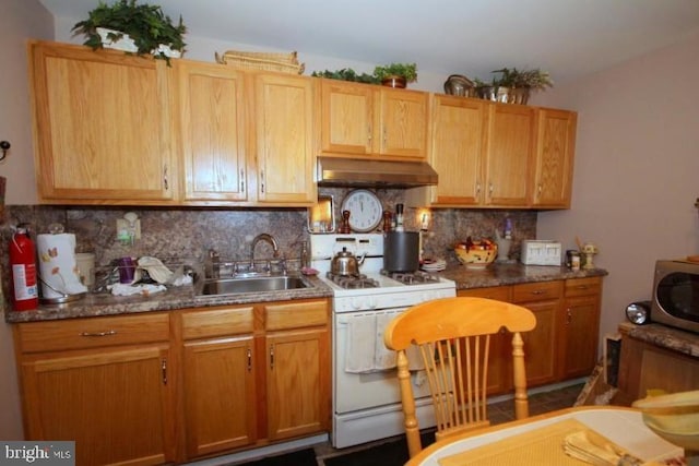 kitchen with dark stone countertops, backsplash, white range with gas stovetop, and sink