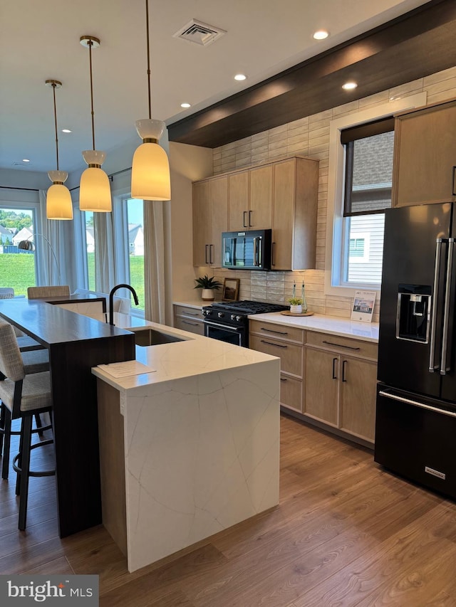 kitchen featuring wood finished floors, a sink, visible vents, black appliances, and an island with sink