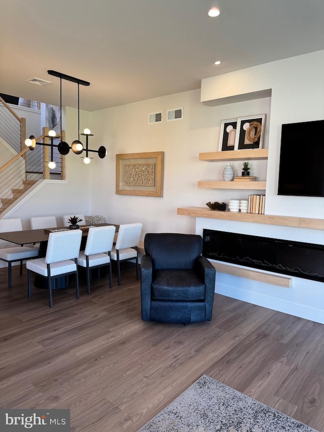 living area with stairs, visible vents, a chandelier, and wood finished floors